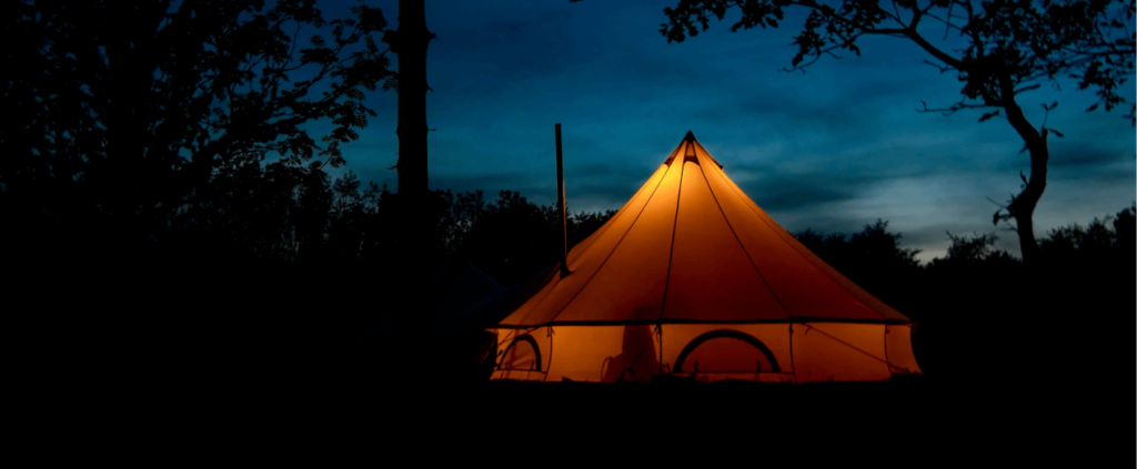 Midnight camping in a deep forest with a tent softly lit from within, surrounded by dark trees and the calm of the night.